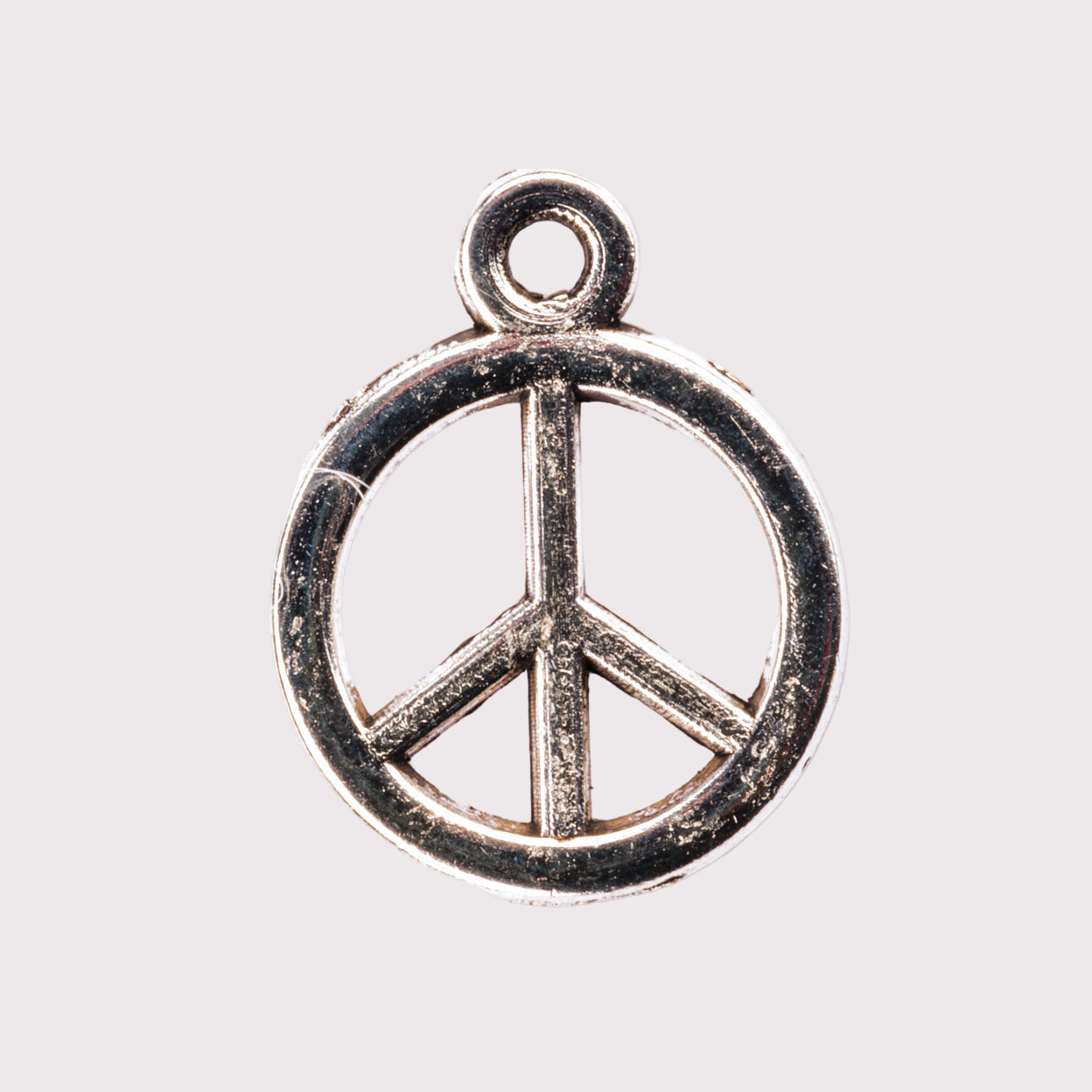 A silver peace sign charm on a white background