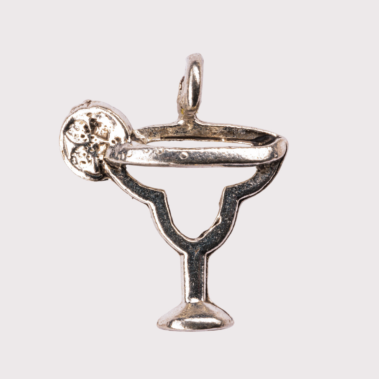 A silver charm in the shape of a margarita glass with a salted rim and a lemon slice on the side.